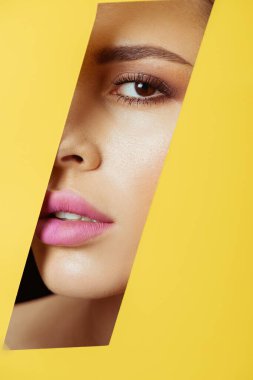 Woman with makeup looking at camera across quadrangular hole in yellow paper clipart