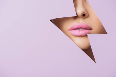 Cropped view of female face with pink lips in hole in violet paper clipart
