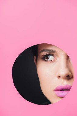 Duman gibi gözleri ve pembe dudakları olan güzel bir kız siyah arka planda kağıtta yuvarlak bir deliğe bakıyor.