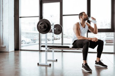 Yakışıklı sporcu spor salonunda halterin yanında protein milkshake içiyor. 