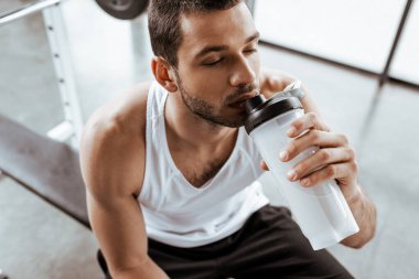 Spor salonunda elinde spor şişesi tutarken protein milkshake içen sporcunun genel görünümü 