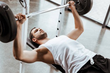 Spor salonunda halterle egzersiz yapan yakışıklı sporcunun seçici odağı. 