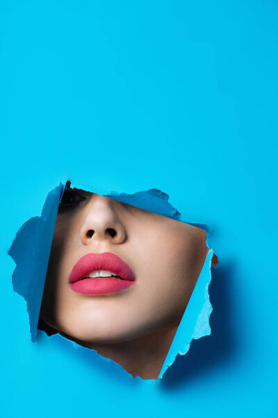 Woman with pink lips looking across hole in blue paper