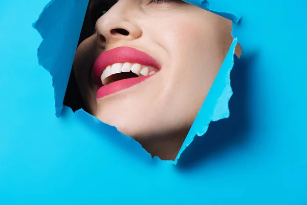 Szczęśliwa Kobieta Różowymi Ustami Uśmiechnięta Przez Rozdarty Niebieski Papier — Zdjęcie stockowe
