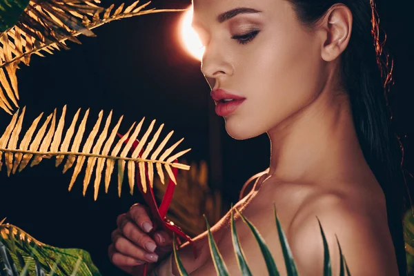 Siyah arka plandaki yaprakların yakınındaki anthurium 'a bakan seksi kadın.