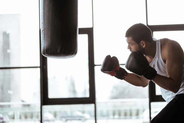 パンチバッグ付きボクシンググローブトレーニングのハンサムなスポーツマンの側面図 — ストック写真