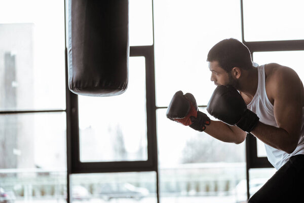 вид сбоку красивого спортсмена в боксёрских перчатках с боксерской грушей
  