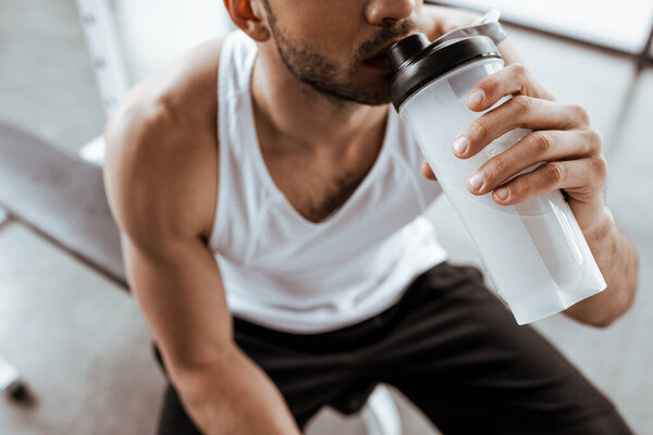 cropped view of sportsman drinking protein milkshake while holding sports bottle 