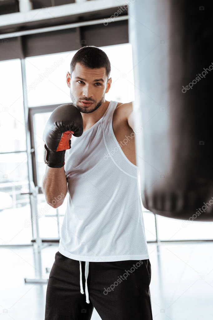 selective focus of handsome man in boxing gloves exercising with punching bag  