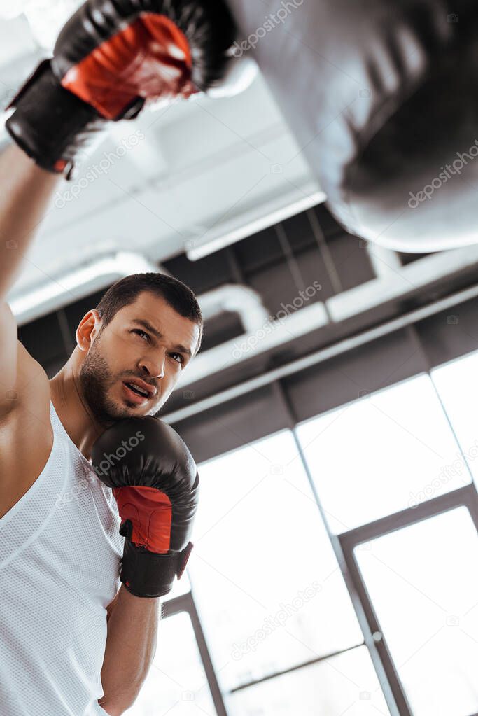selective focus of sportsman in boxing gloves exercising with punching bag  