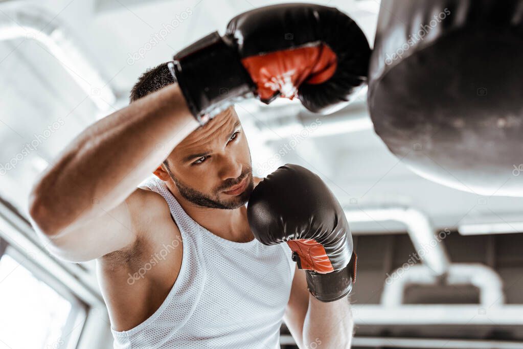 selective focus of handsome sportsman in boxing gloves training with punching bag  