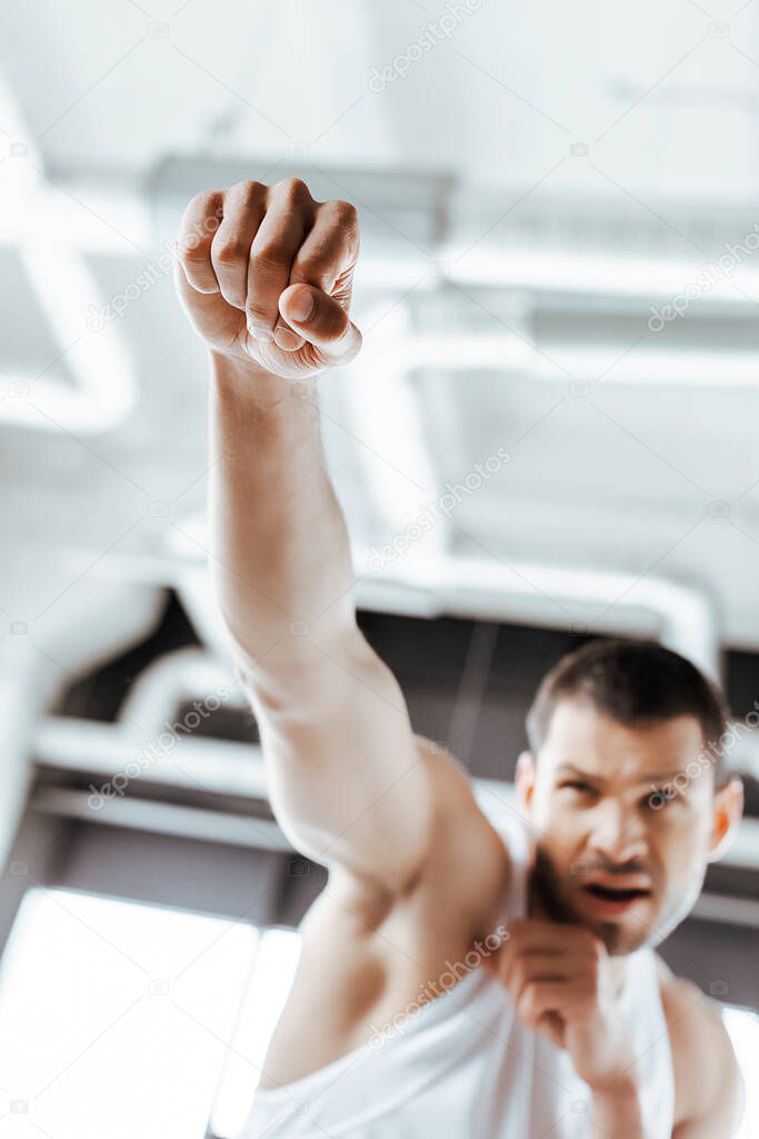 selective focus of emotional fighter with clenched fists training in sports center 