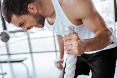 selective focus of emotional man screaming while exercising with battle ropes clipart