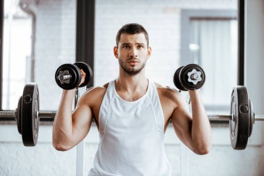 Spor salonunda spor yaparken elinde dambıl tutan sporcu.  
