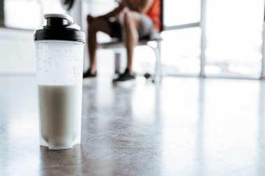 Spor salonundaki sporcunun yanında protein milkshake ile spor şişesinin seçici odağı. 