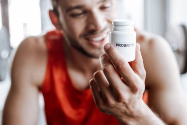Spor salonundaki probiyotik harflerle dolu şişeyi tutan mutlu sporcunun seçici odağı. 