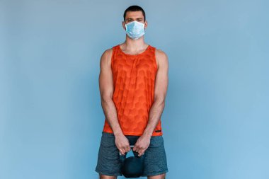 Sağlık maskeli bir sporcu mavi halterde halterle çalışıyor. 