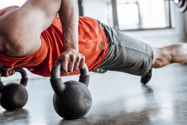 cropped view of athletic sportsman doing plank exercise with heavy dumbbells 