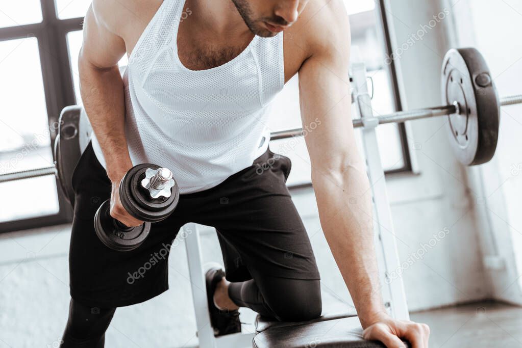 cropped view of bearded man exercising with heavy dumbbell in gym  