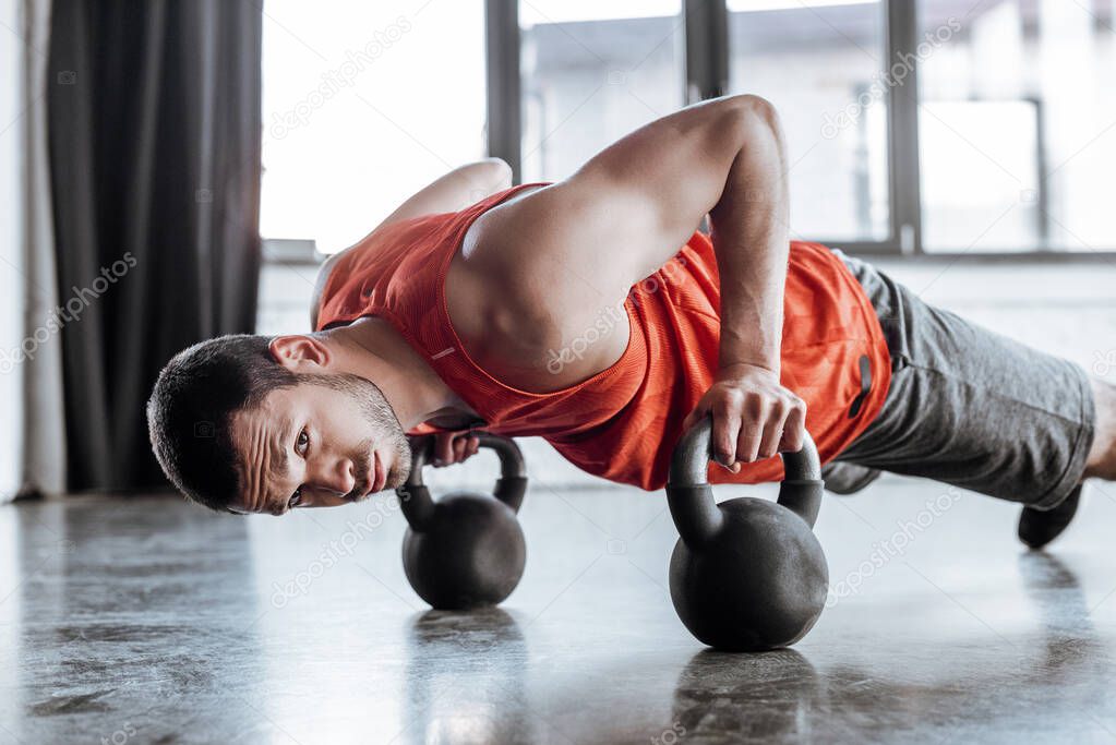 strong sportsman doing plank exercise with heavy dumbbells and looking at camera