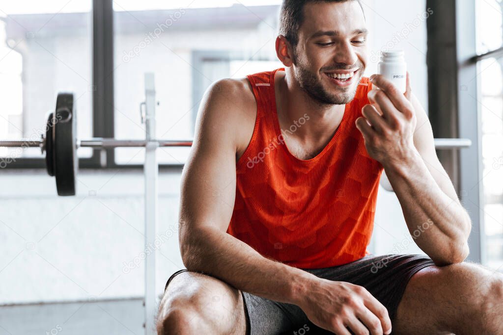 happy sportsman looking at bottle with probiotic lettering in gym 