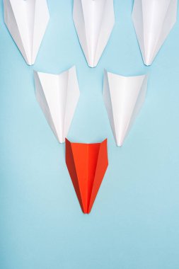 Top view of unique red paper plane among white on blue background clipart