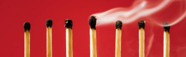 Unique burned match with smoke among another on red, panoramic shot clipart