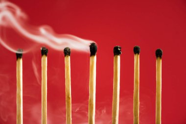 Unique burned match with smoke among another on red clipart