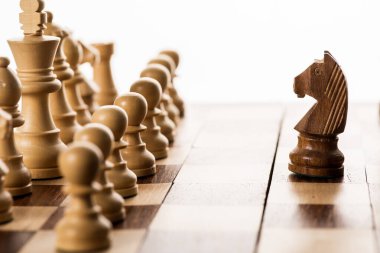 Selective focus of brown knight against chess pieces on chessboard isolated on white clipart