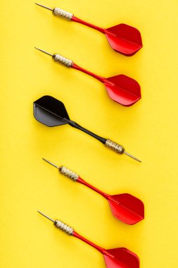 Flat lay with unique black dart among red on yellow clipart