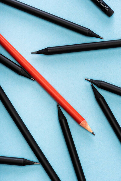 Top view of unique red pencil among black on blue background