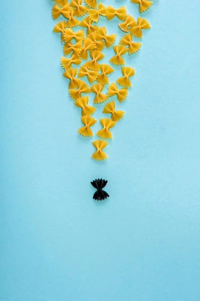 Vista Superior Pasta Negra Única Entre Amarillo Sobre Fondo Azul — Foto de Stock