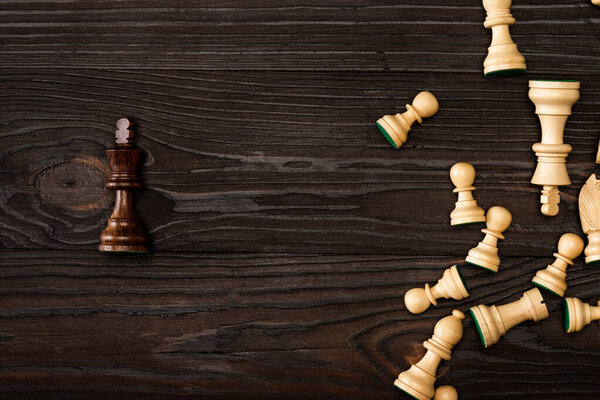 Top view of unique brown king with white chess pieces on wooden background