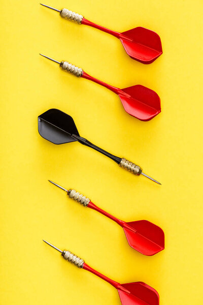 Flat lay with unique black dart among red on yellow