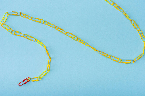 High angle view of chain with unique red and yellow paper clips on blue