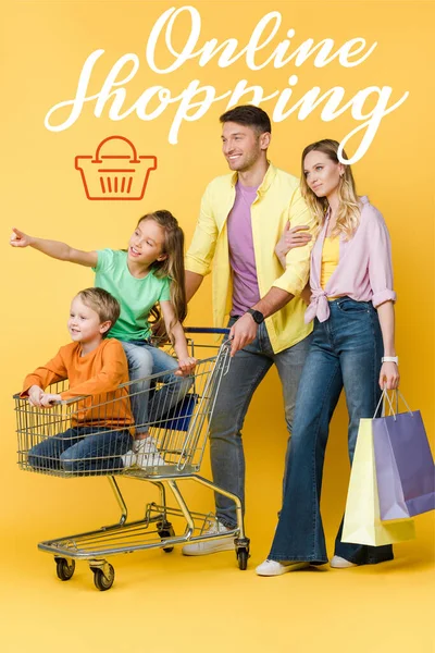 父母们拿着购物袋 孩子们摆着姿势 坐在黄色的网上购物车里 — 图库照片