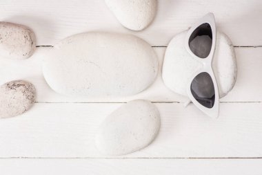 Top view of sea stones with sunglasses on white wooden surface clipart