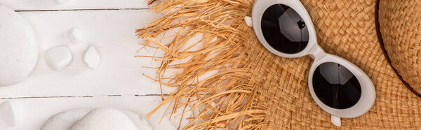 Panoramic shot of top view of straw hat with sunglasses and pebbles on white wooden surface