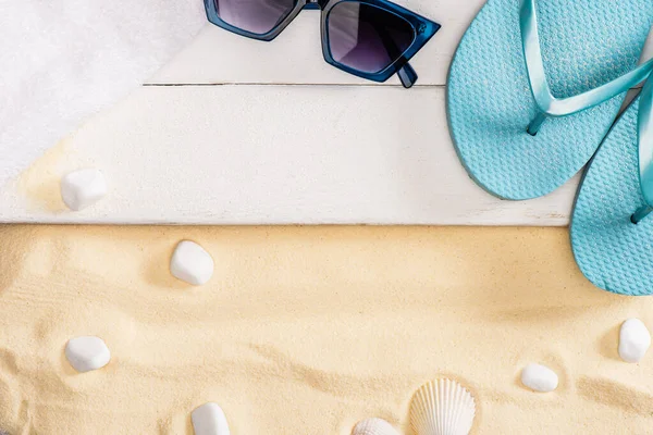 太阳镜附近的蓝色翻筋斗和沙滩上卵石附近的白色木板上的毛巾的顶部视图 — 图库照片