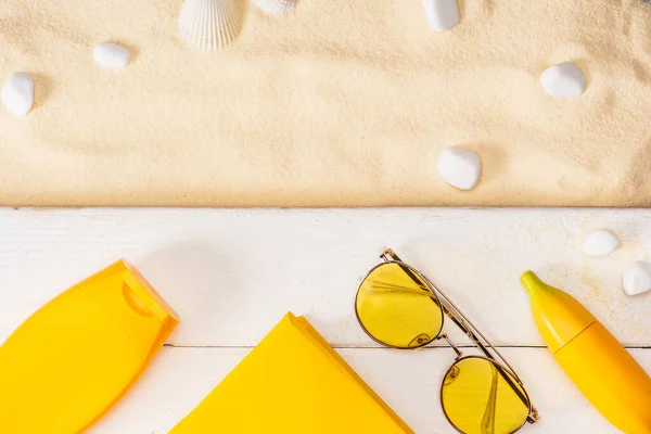 黄色的防晒霜 书籍和太阳镜在靠近海石的白色木板和沙滩上的海贝壳上的顶部视图 — 图库照片