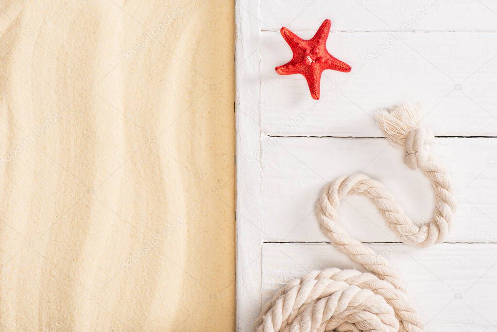 Top view of red starfish near rope on white wooden planks near sand