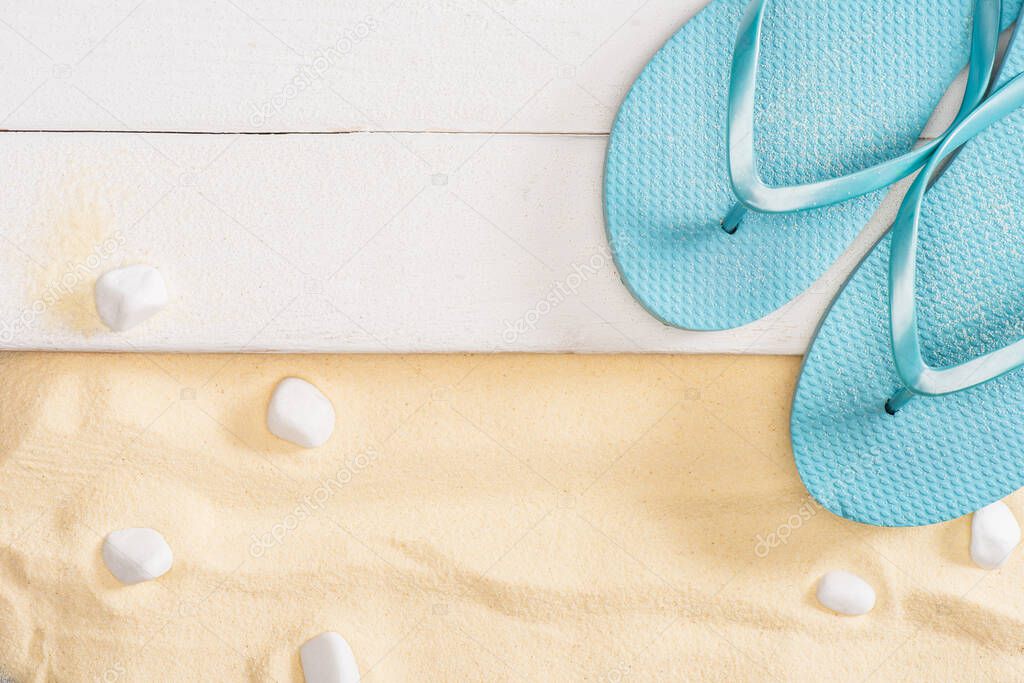 Top view of blue flip flops on white wooden planks and pebbles on sand