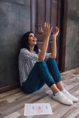 Elleri havada stresli bir kadın odanın duvarının yanında yere bakıyor.
