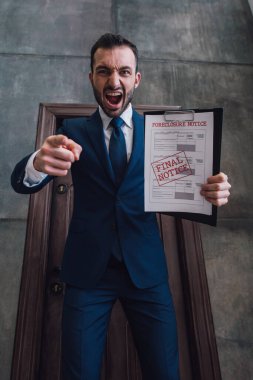 Low angle view of aggressive collector with documents with foreclosure and final notice lettering pointing with finger and shouting in room clipart