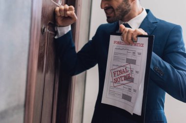 Cropped view of angry collector with documents with foreclosure and final notice lettering knocking on door clipart