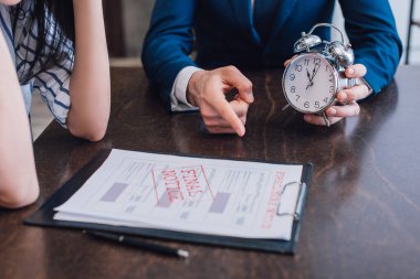 Cropped view of collector with alarm clock pointing at documents with foreclosure and final notice lettering near woman at table clipart