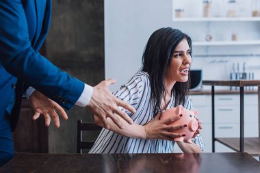 Collector pulling hands to woman with piggy bank at table in room clipart