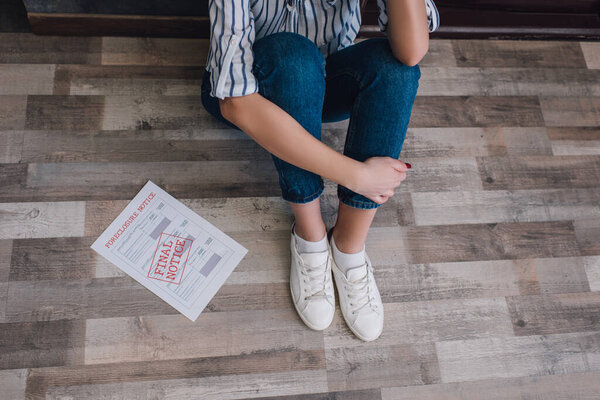 Обрезанный вид женщины, сидящей на полу рядом с документом с печатью с окончательным надписью в комнате
