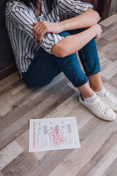 Обрезанный вид женщины, сидящей на полу рядом с документом с лишением права выкупа и надписью в комнате
