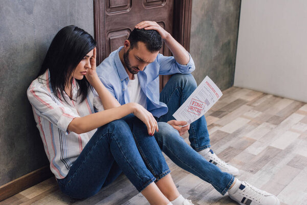 Разочарованные банкроты держат документ с окончательным уведомлением надпись на полу возле стены в комнате
